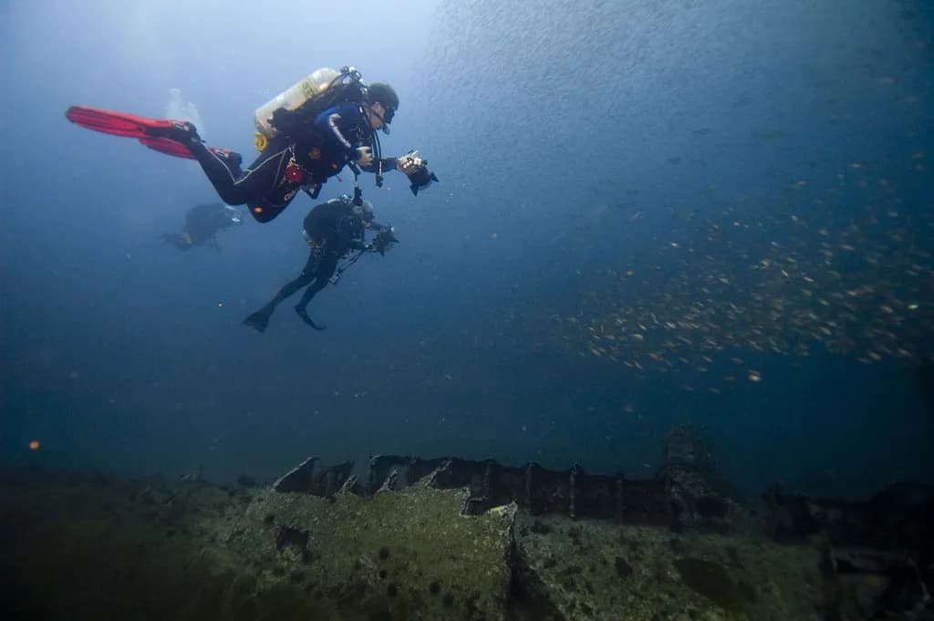 A marine researcher in scuba gear conducting an underwater reef survey with a slate and camera