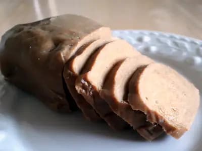A poached seitan log part sliced on a plate, showing the dense fibrous interior that wheat gluten develops