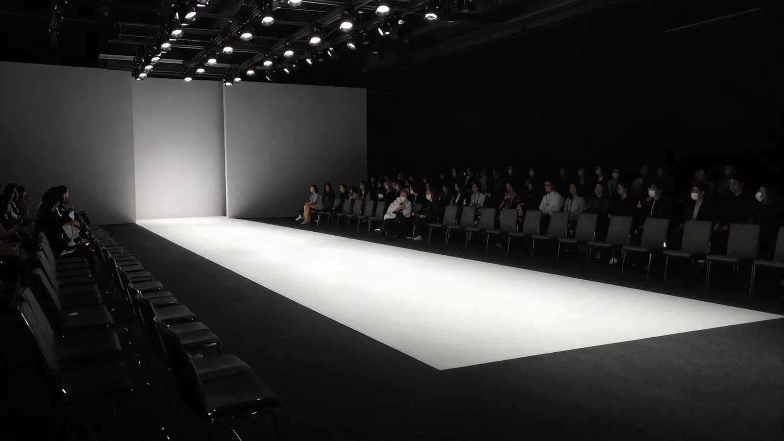 A lit empty runway with the audience seated on either side before a show