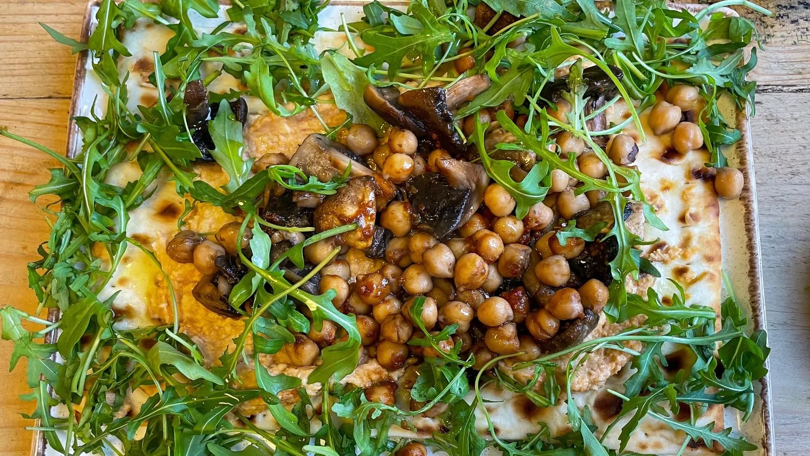 A flatbread topped with roasted mushrooms, chickpeas and rocket, photographed at a delicatessen. It is not the dish in this recipe but it is the same construction