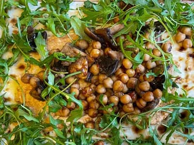 A flatbread topped with roasted mushrooms, chickpeas and rocket, photographed at a delicatessen. It is not the dish in this recipe but it is the same construction