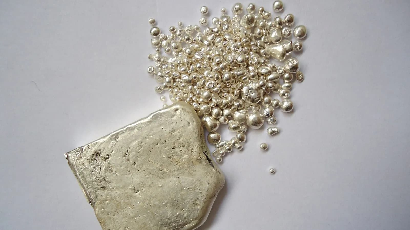 A cast silver ingot beside a scattering of silver granules