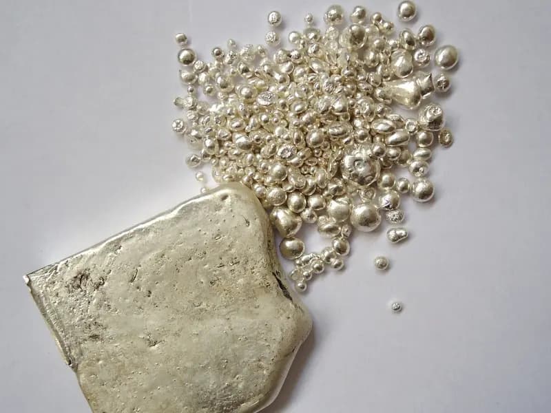 A cast silver ingot beside a scattering of silver granules