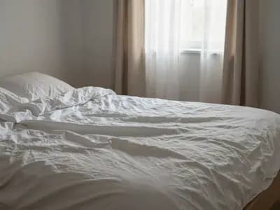 An unmade bed with morning light falling across the linen