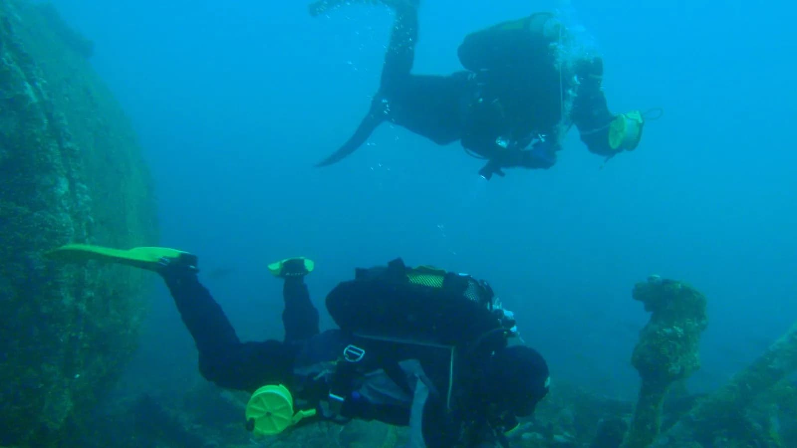 A scuba diver preparing to deploy a delayed surface marker buoy at depth, beside the boiler of a wreck