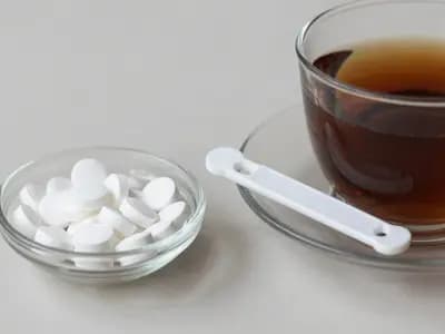 Sweetener tablets and a dispenser beside a cup of tea