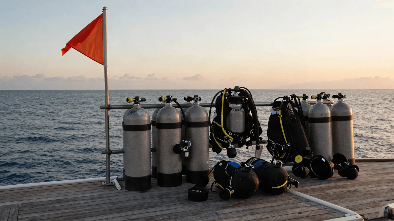 Scuba cylinders and kit lined up on a dive boat deck at sunrise
