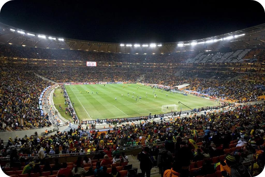 A packed stadium crowd at a World Cup match with fans in team colors under stadium lights