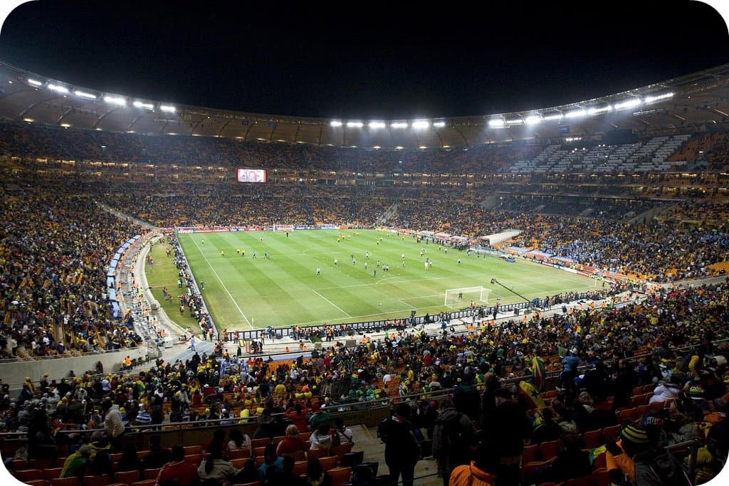 A packed stadium crowd at a World Cup match with fans in team colors under stadium lights