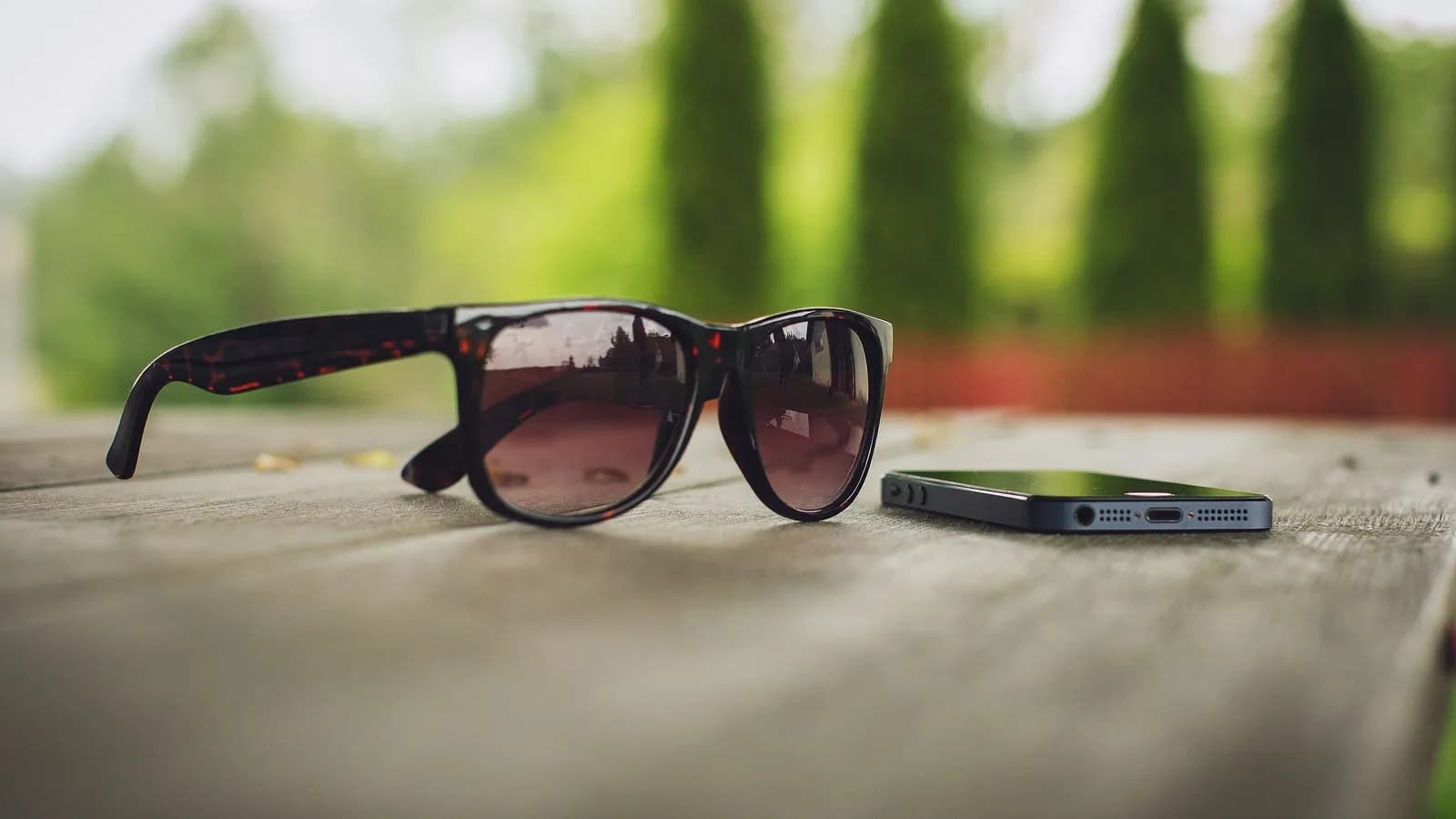 A pair of sunglasses and a phone on a wooden table outdoors
