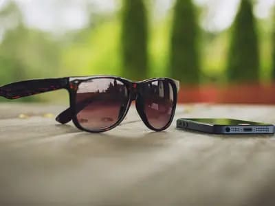 A pair of sunglasses and a phone on a wooden table outdoors
