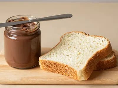 An unbranded jar of chocolate spread beside sliced bread