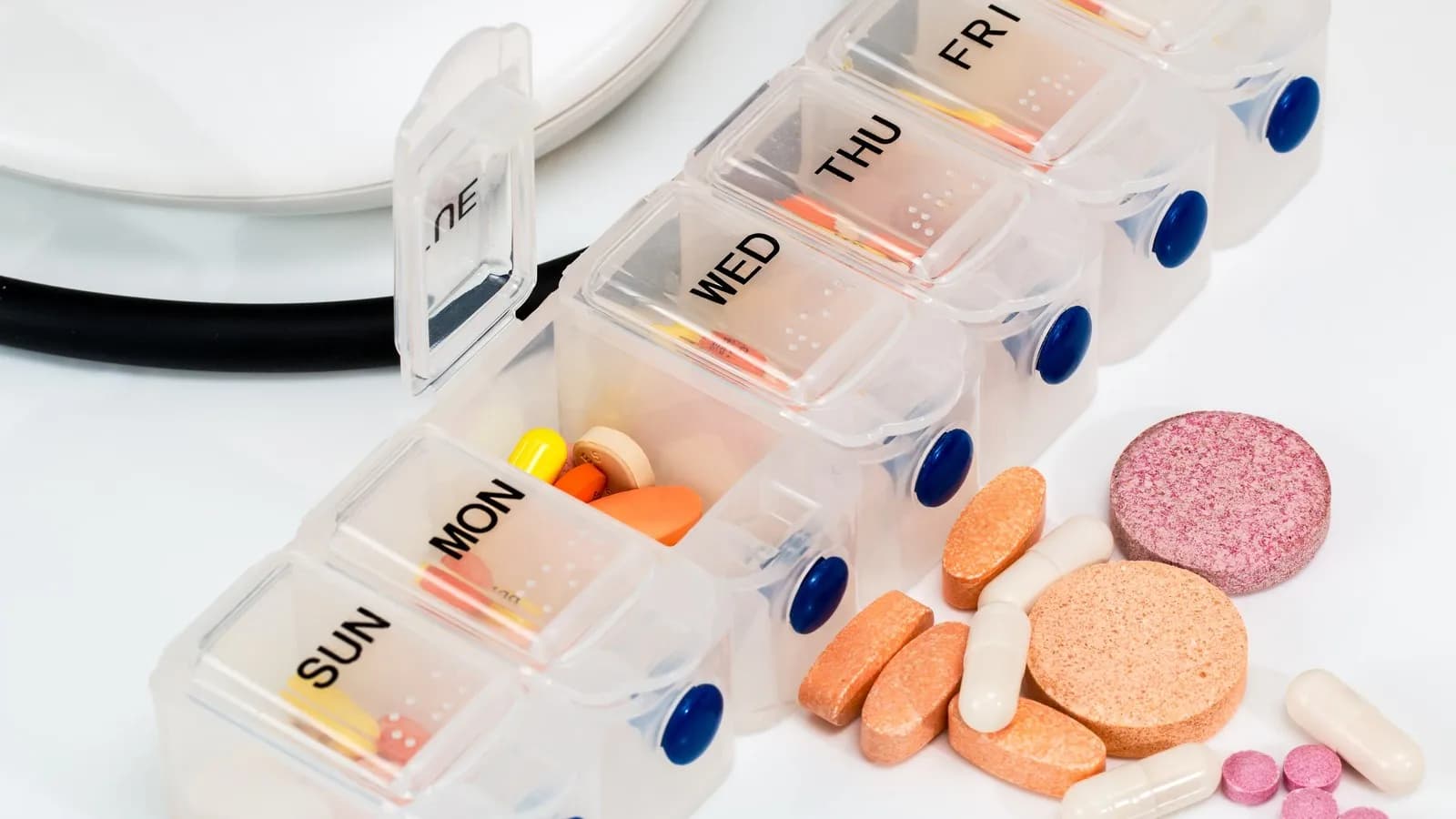 A weekly pill organiser beside loose tablets and capsules, illustrative of everyday prescription and over-the-counter medicines and not a particular treatment, photographed in December 2017