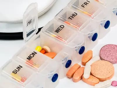 A weekly pill organiser beside loose tablets and capsules, illustrative of everyday prescription and over-the-counter medicines and not a particular treatment, photographed in December 2017