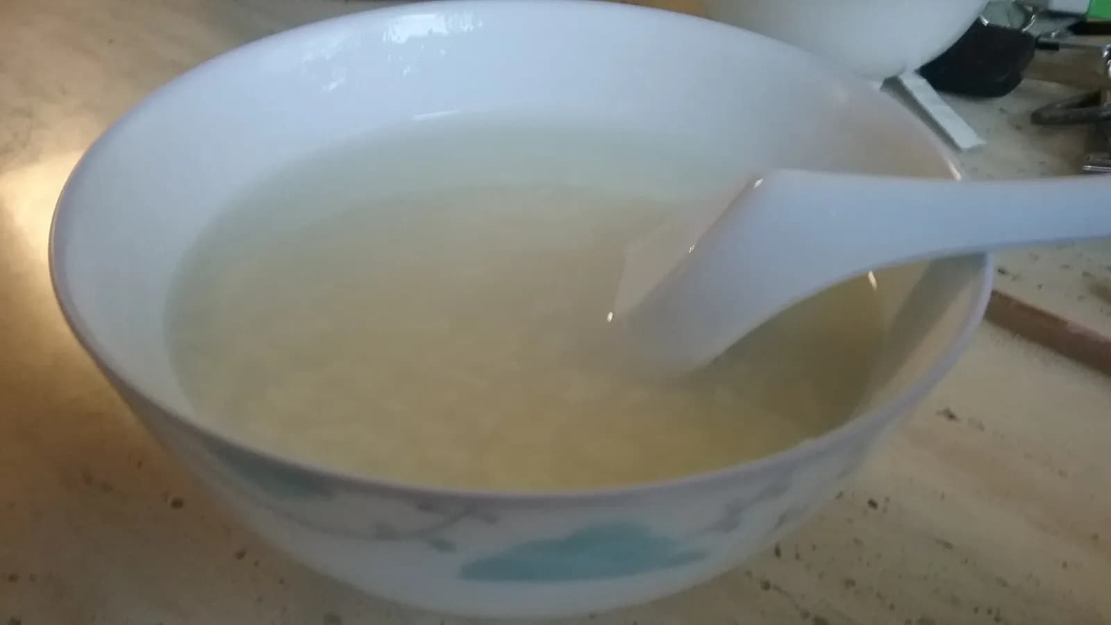 A bowl of plain white congee with a spoon resting in it, the rice grains cooked down until they have almost disappeared into the liquid