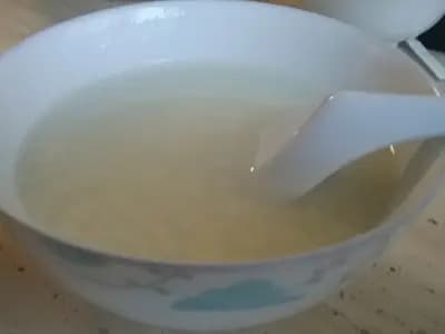 A bowl of plain white congee with a spoon resting in it, the rice grains cooked down until they have almost disappeared into the liquid