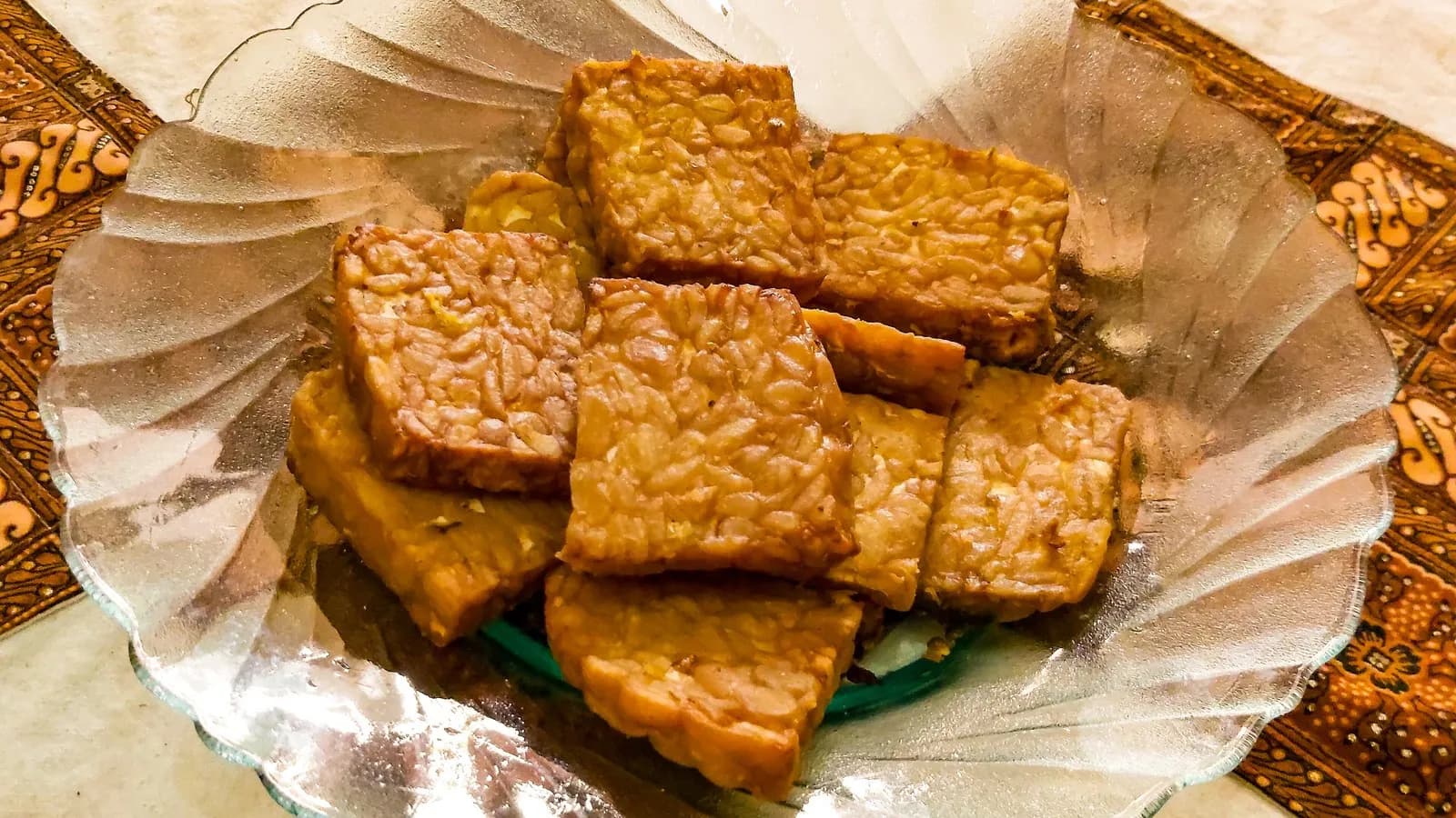 Slices of fried tempeh arranged on a plate, the individual soybeans still visible in the cake where the mould has bound them together