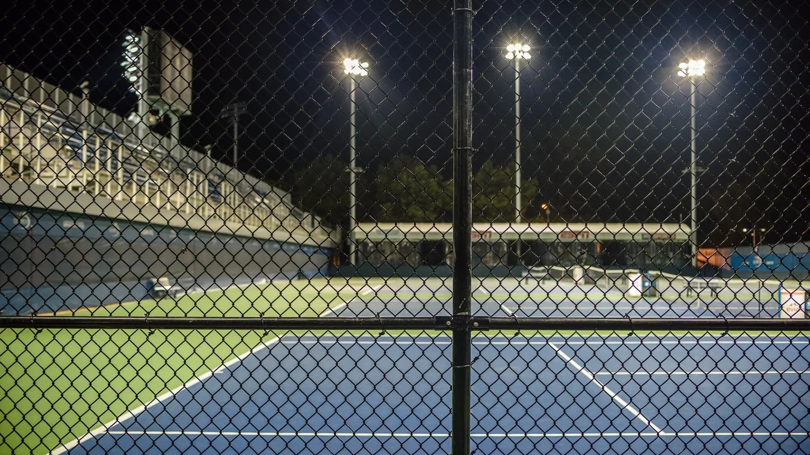 Hard courts at the US Open site in Flushing Meadows at night, seen through a perimeter fence