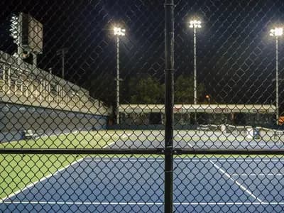 Hard courts at the US Open site in Flushing Meadows at night, seen through a perimeter fence