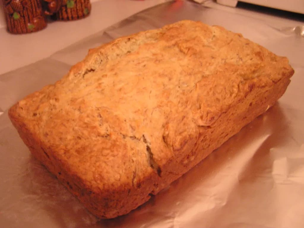 A thick slice of golden vegan banana bread with a moist crumb, served on a plate with a knife
