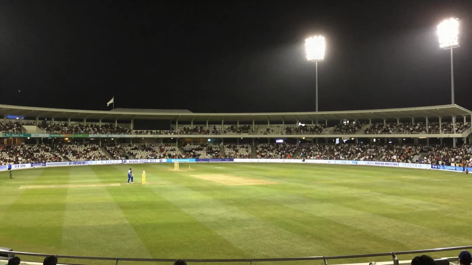 A floodlit cricket stadium during an evening match