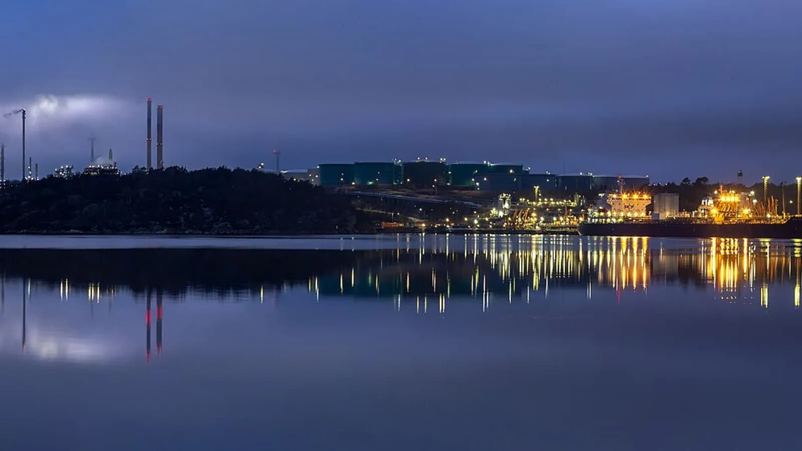 An oil refinery with tall process towers and lit storage areas across a calm inlet at blue hour, the Preemraff refinery at Brofjorden, Sweden, photographed on 4 November 2021, a file photograph illustrative of a refinery and not of Ras Tanura or of any Saudi facility