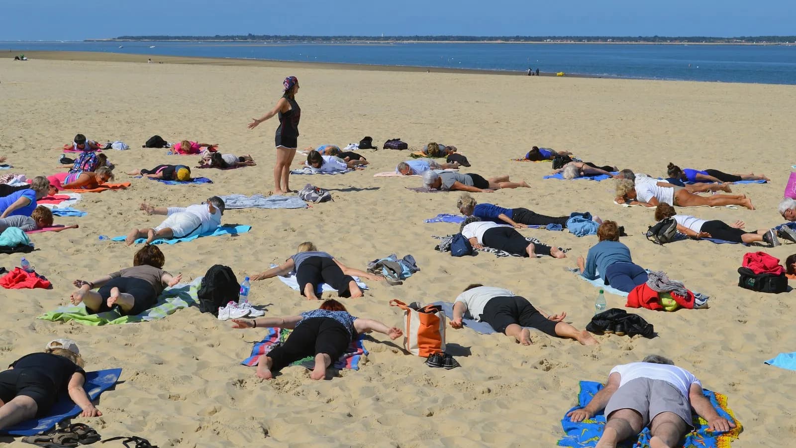 A large outdoor yoga class on a beach, participants spread across the sand following a teacher